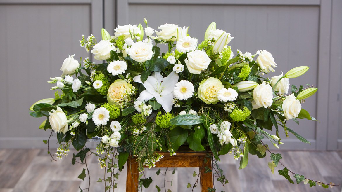 Composition florale pour poser sur le cercueil. Roses blanches, lys et verdure - Schilliger Fleurs