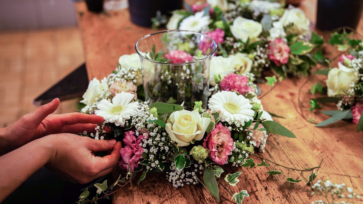 Couronne de fleurs composé de roses blanches, de marguerites, de lierre et de gypsophile qui entoure un vase - Schilliger Fleurs  - Fleuriste à Gland (La Côte, Vaud)